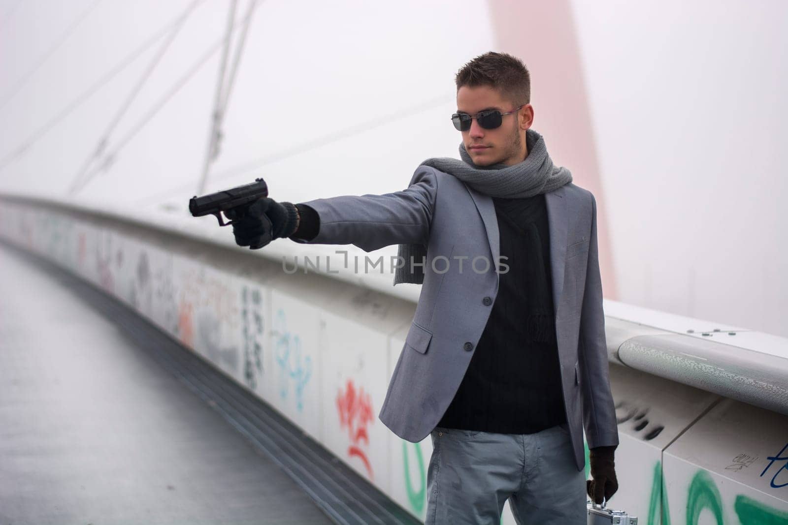 Well dressed handsome young detective or policeman or mobster standing in an urban environment aiming a gun to left side