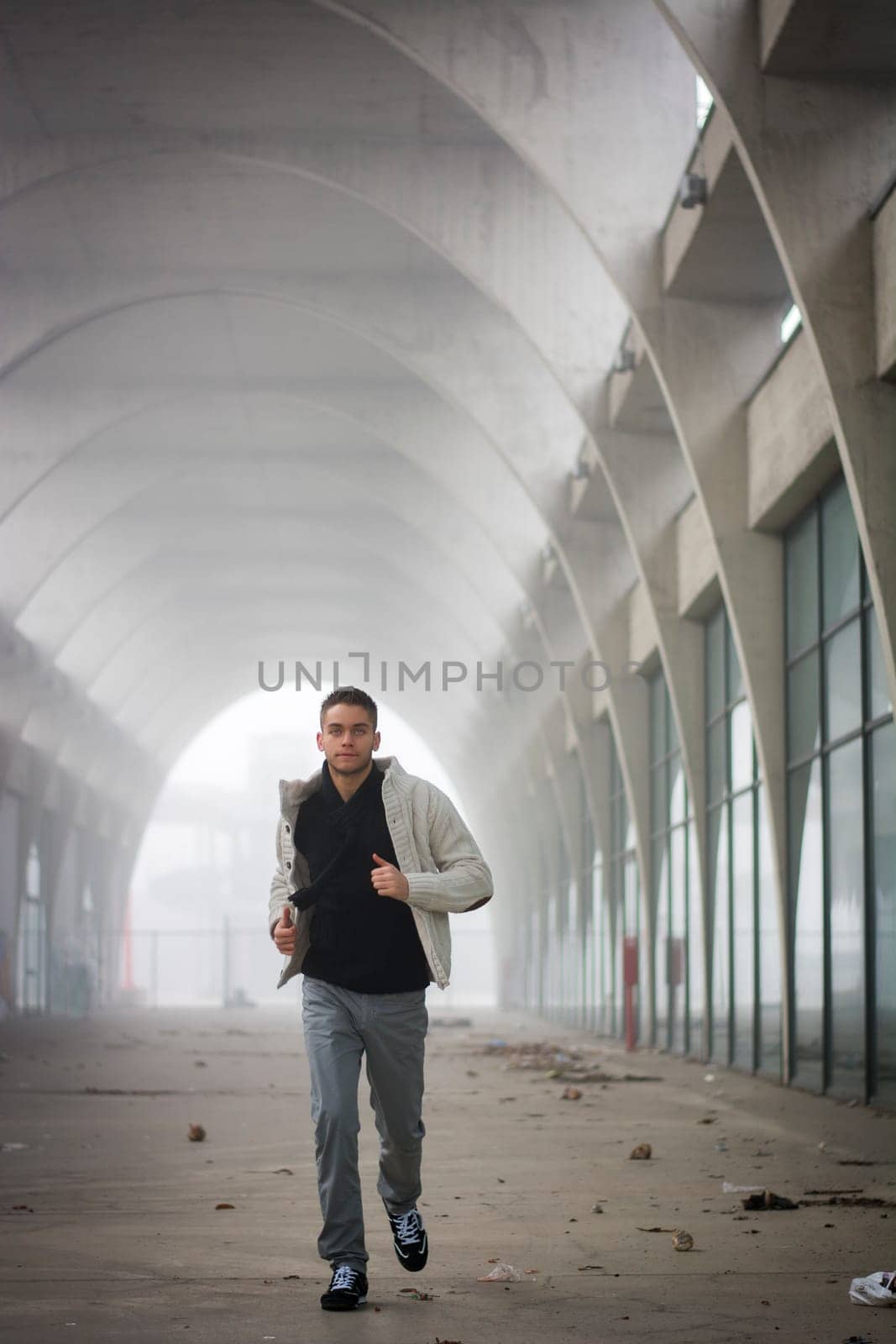 Front View of Young Man Running Through Abandoned Arched Tunnel Towards Camera