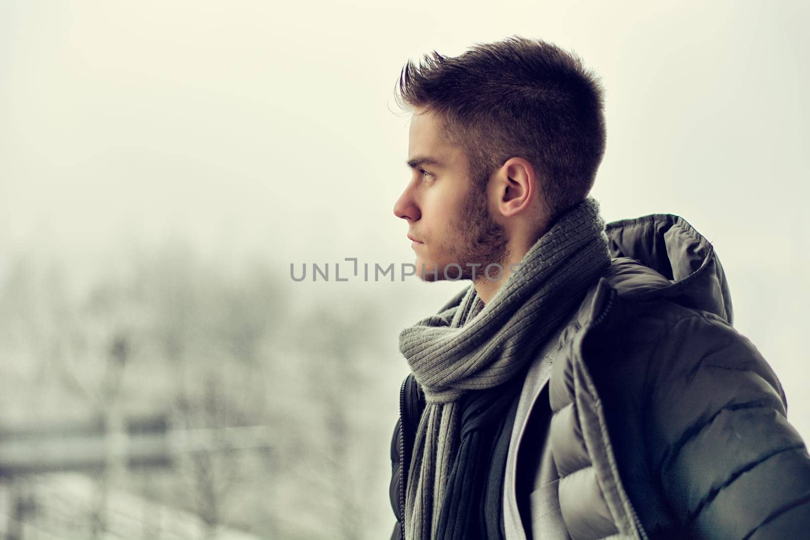 Profile view of handsome young man outdoor in winter wearing scarf, looking away thinking