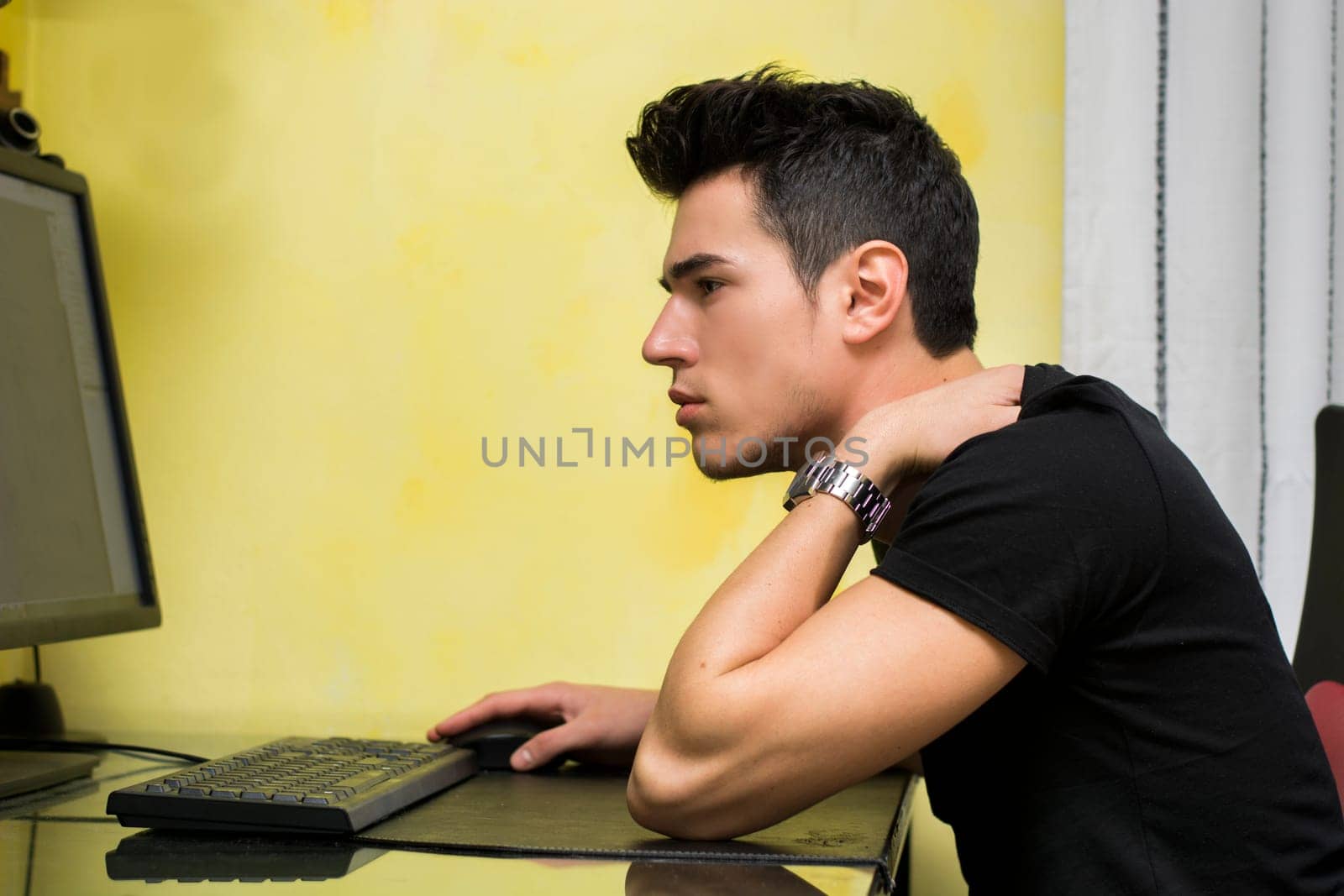 Handsome young man working or studyiing at computer at home or in office, staring at screen with focused expression