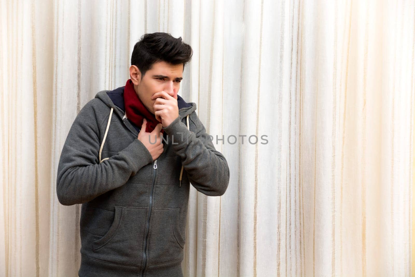 Sick young man with flu or cold, coughing with hand on his mouth. Indoor shot at home