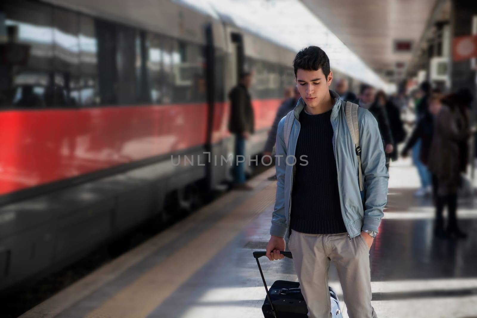 Handsome young male traveler in train station with trolley suitcase, looking down