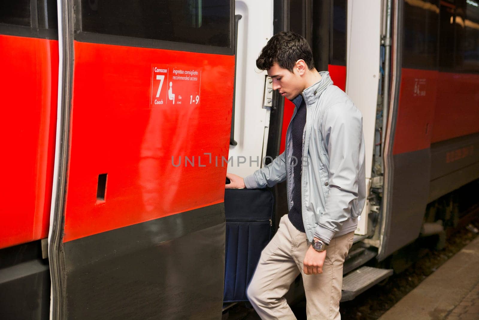 Handsome young man getting aboard on train, standing in open door threshold looking down