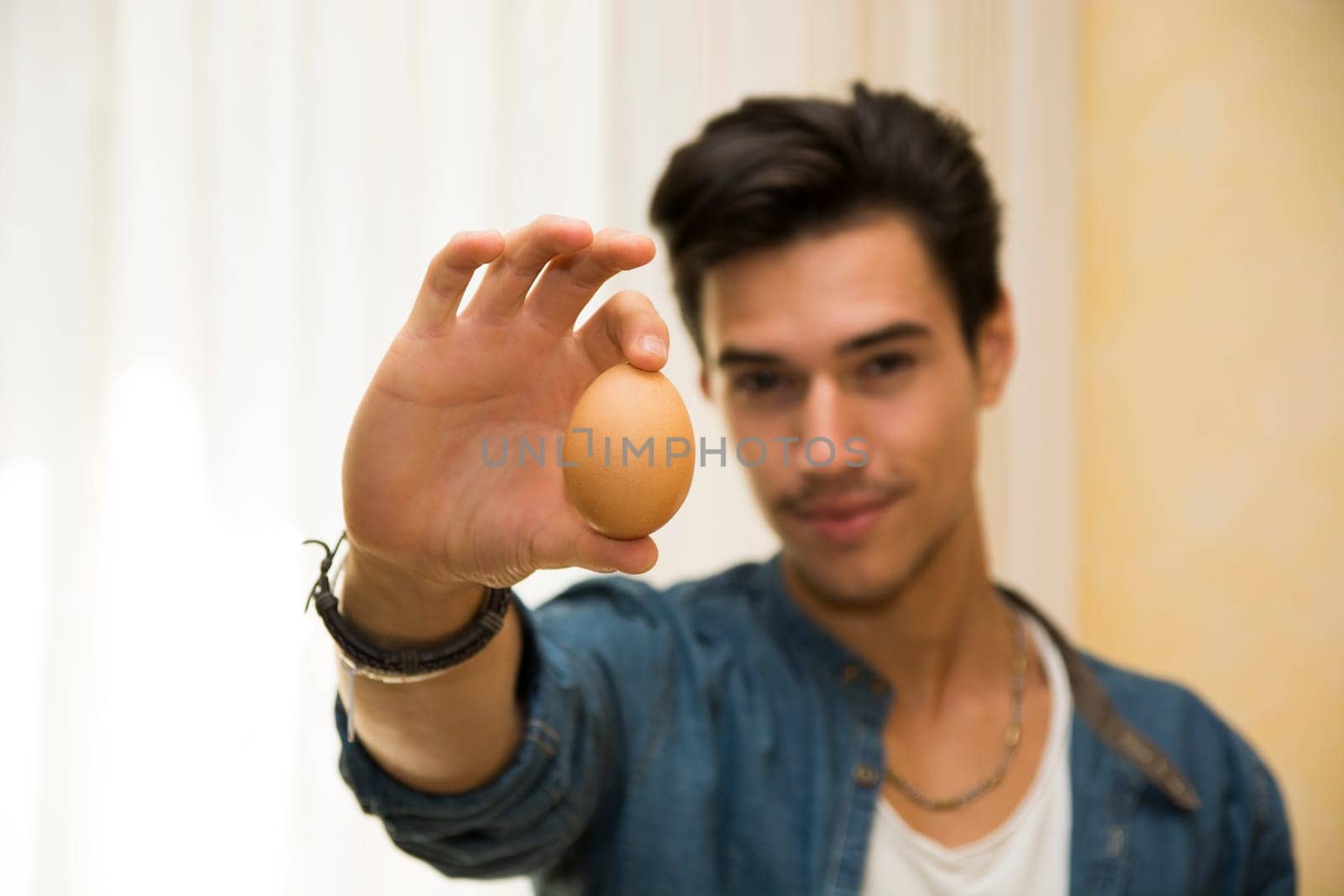 Smiling young man holding an egg in his hand, showing it to the camera