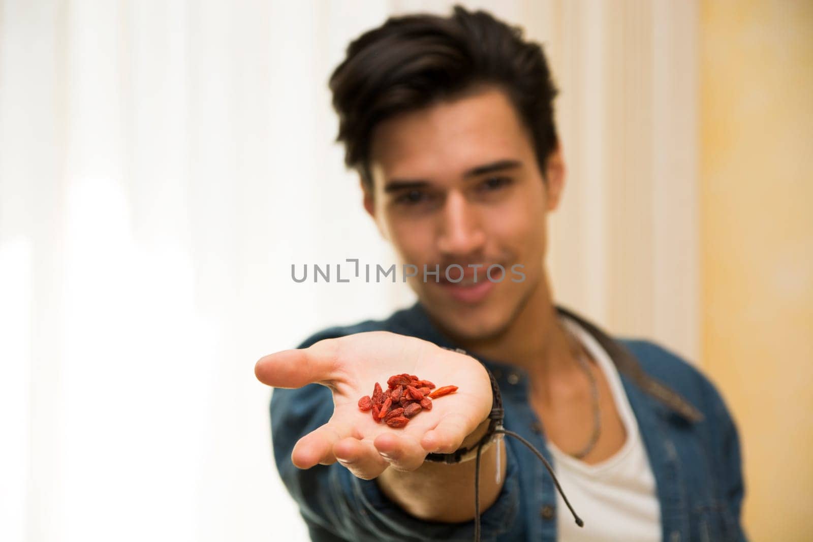 Smiling young man holding goji berries in his hand, showing them to the camera. Focus on the fruits