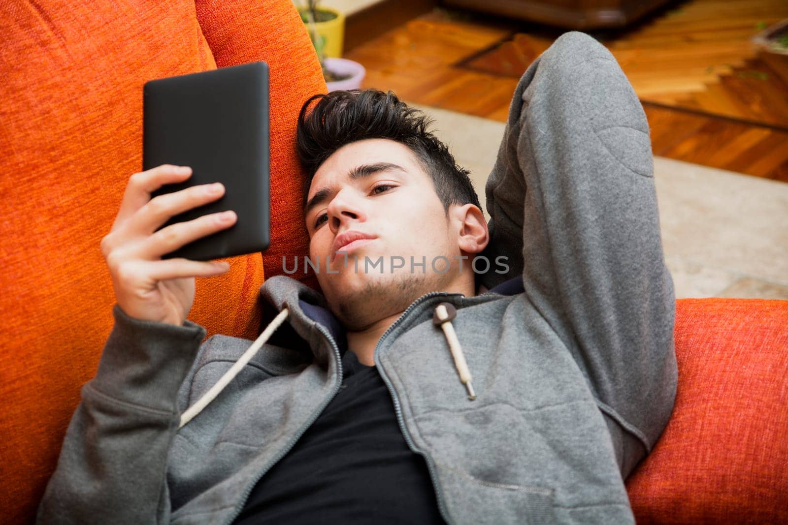 Handsome young man at home reading with ebook reader lying on a couch
