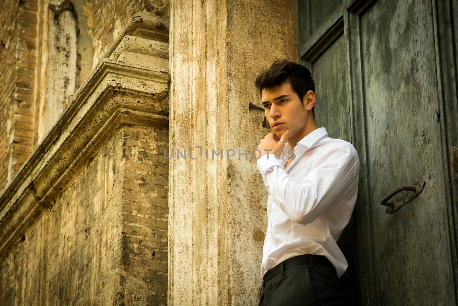 Elegant young man leaning against old wall and door, shot from below
