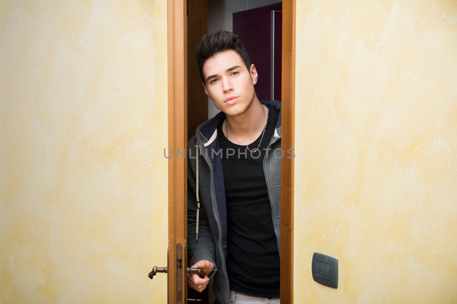 Handsome young man opening door to enter into a room, looking at camera
