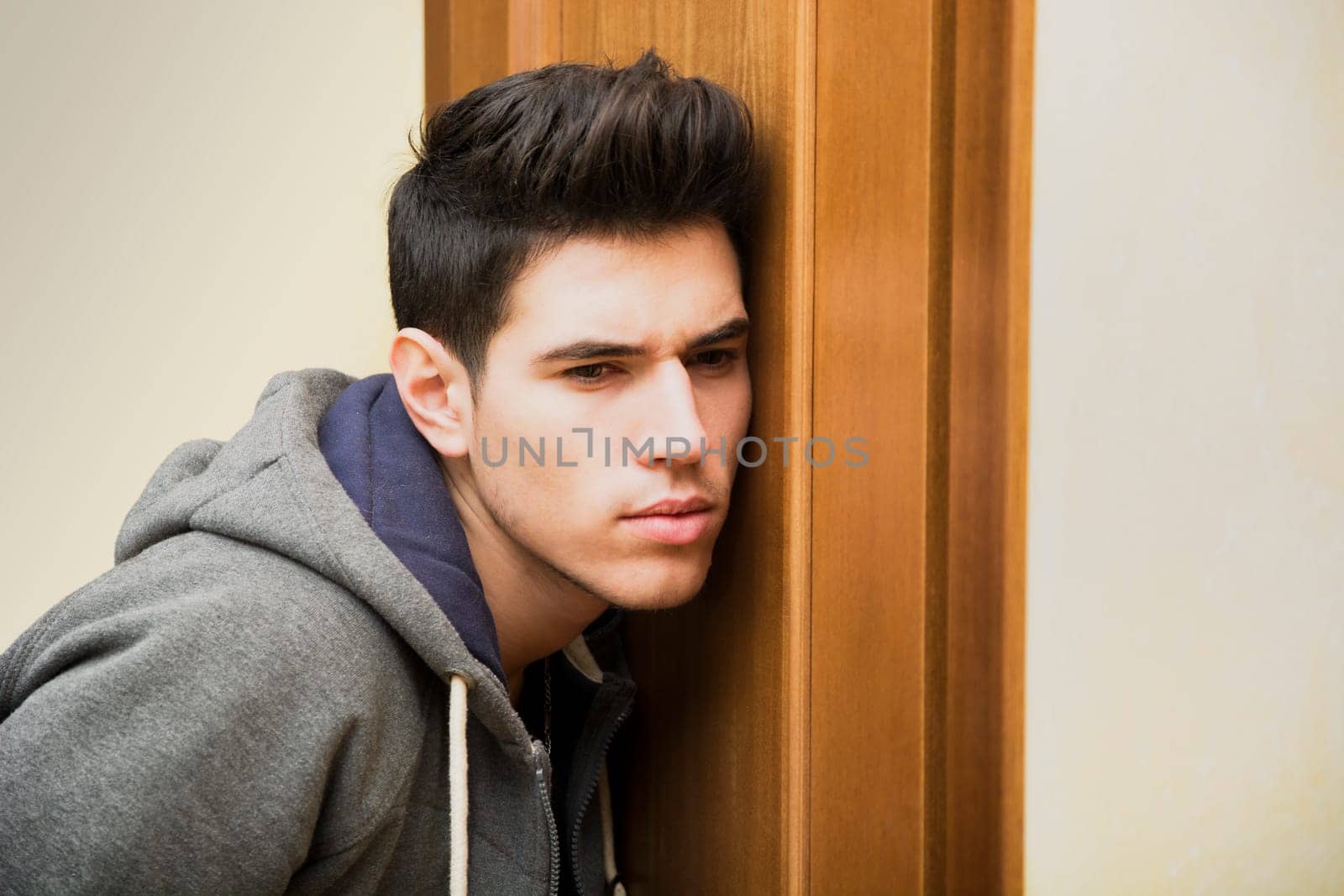 Young man listening in behind a door with a concentrated expression, trying to overhear things
