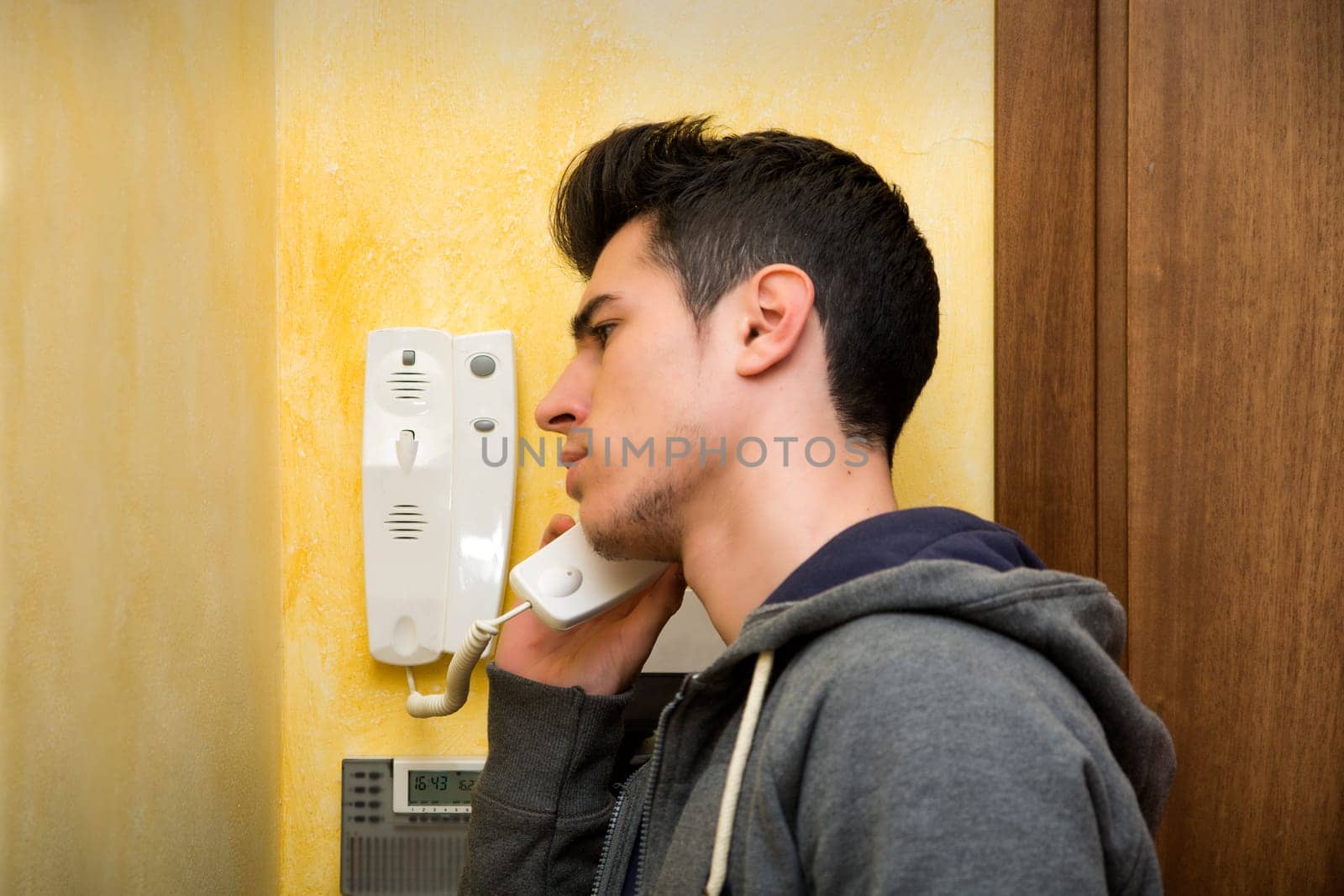 Young man answering the intercom in an apartment, listening to his guests on the other end
