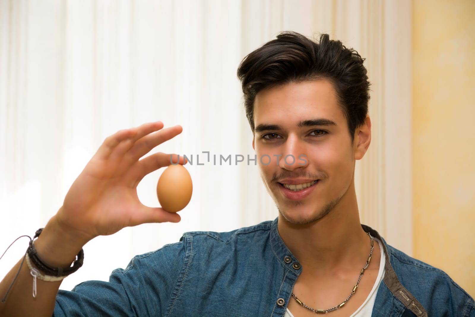 Smiling young man holding an egg in his hand, showing it to the camera