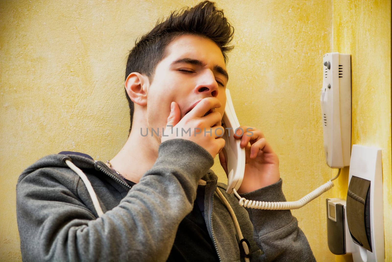 Young man or teenager answering the intercom at the entrance in an apartment yawning