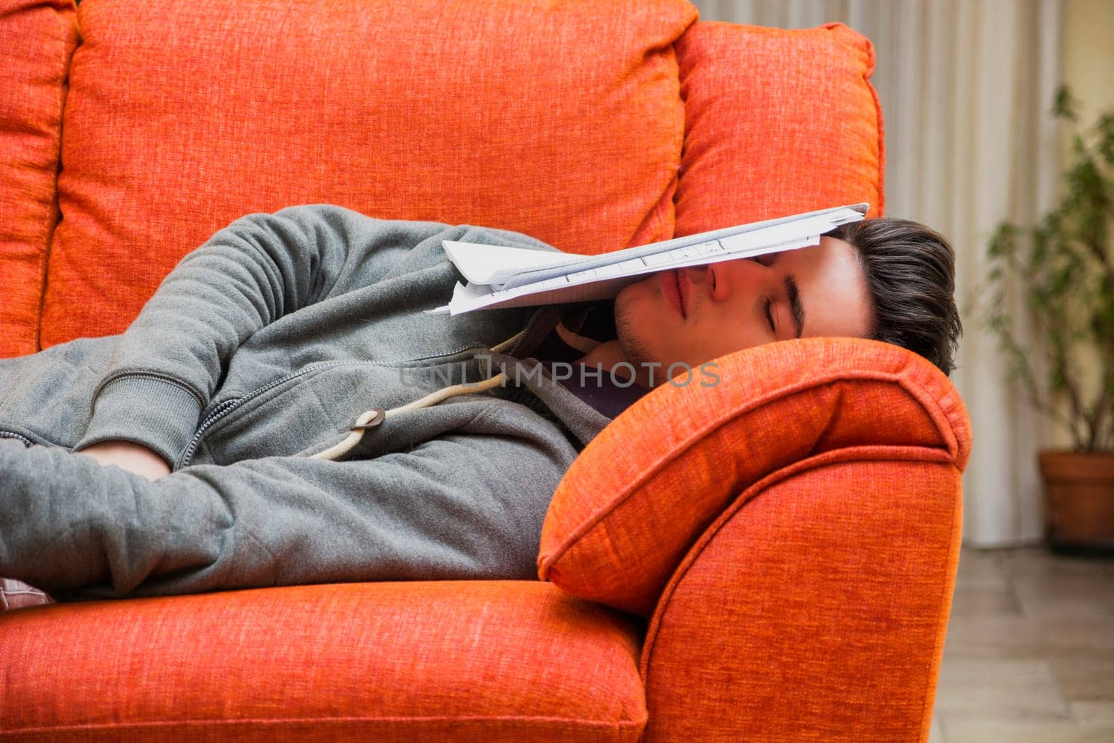 Over-worked, tired young man at home sleeping instead of working or studying, resting with head covered by paper sheets