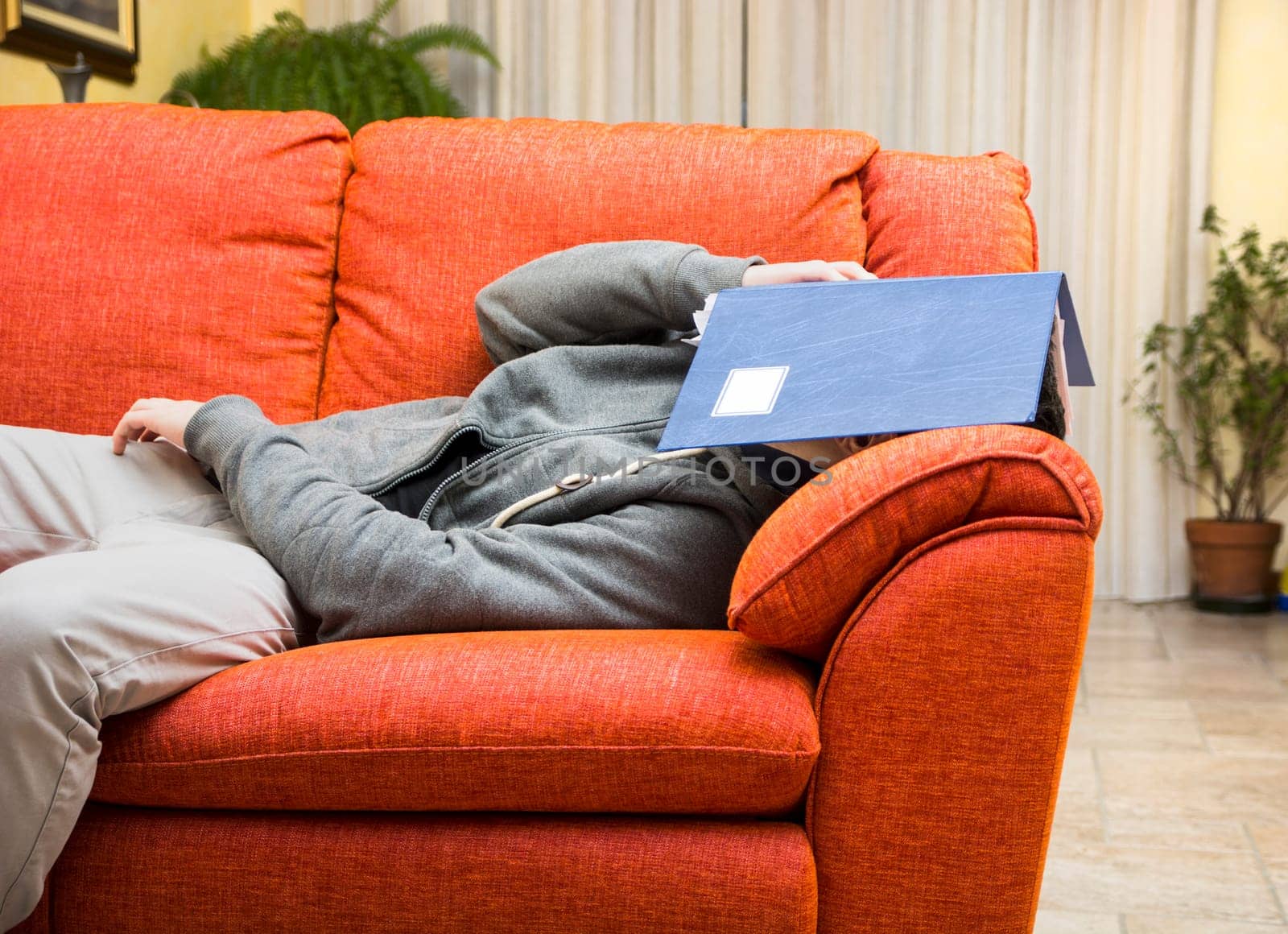 Over-worked, tired young man at home sleeping instead of working or studying, resting with head covered by book