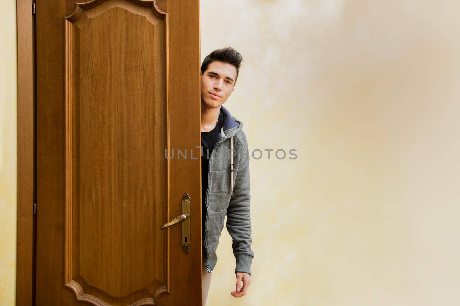 Handsome young man behind open door, getting out, looking at camera with friendly expression