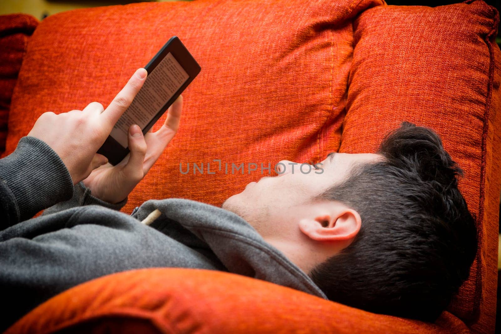 Handsome young man at home reading with ebook reader lying on a couch