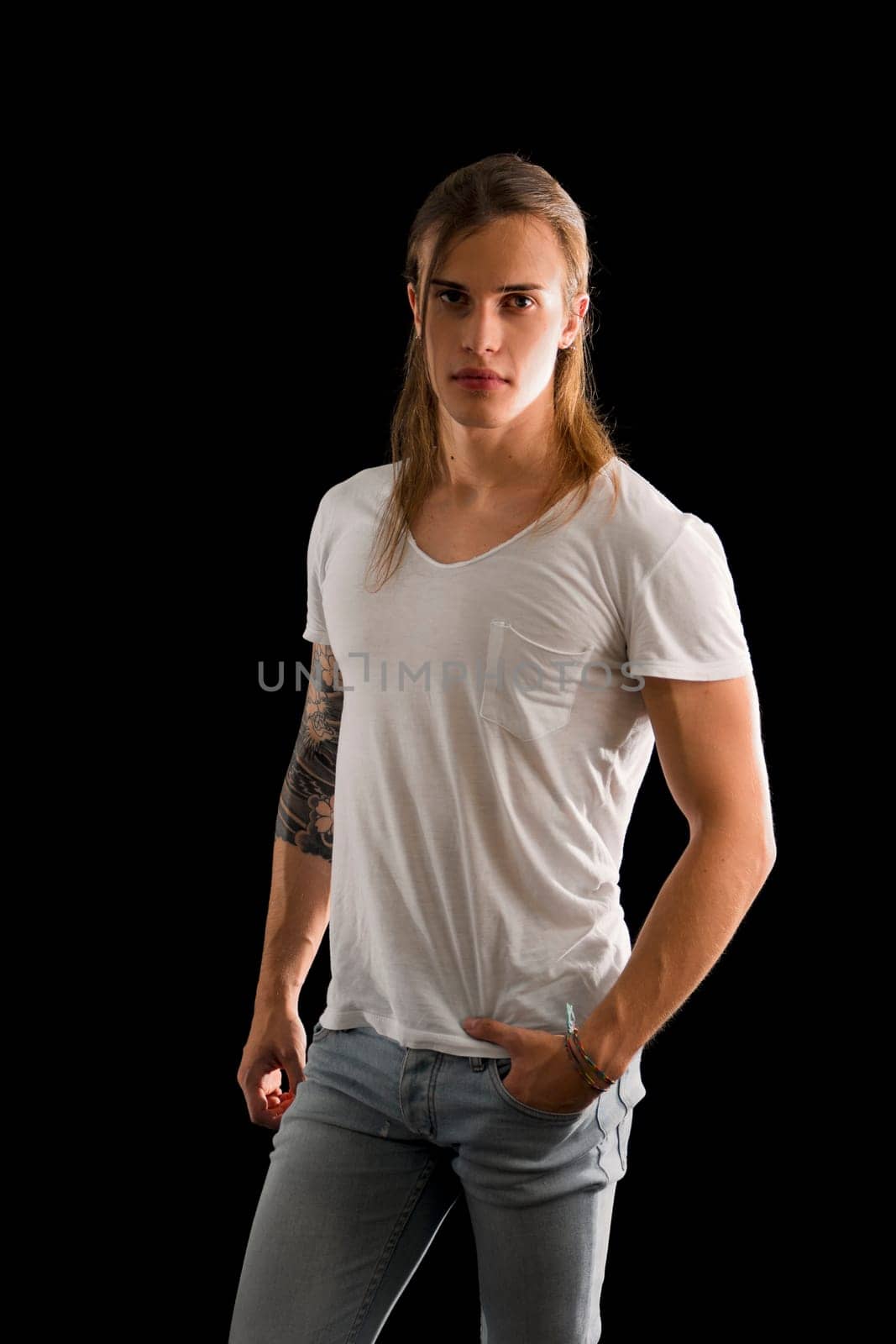Handsome long hair young man isolated on black, looking intensely at camera with confident expression