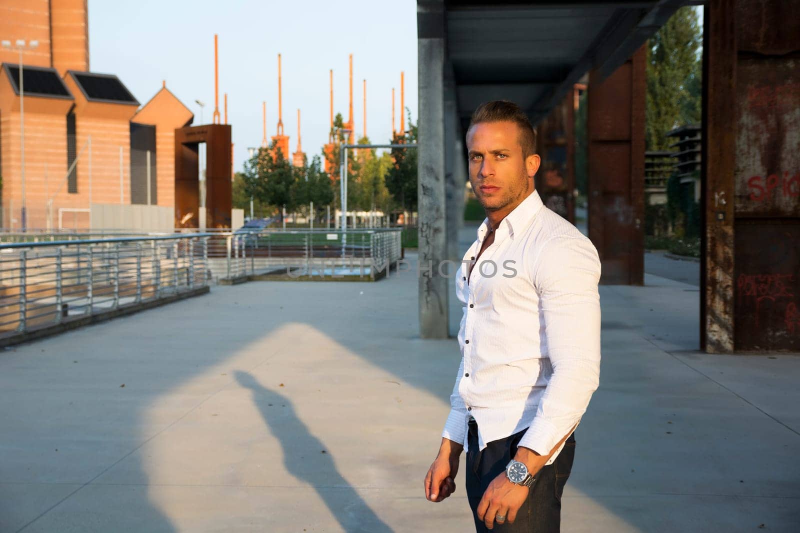 Handsome muscular blond man standing in city setting looking at camera, large copyspace