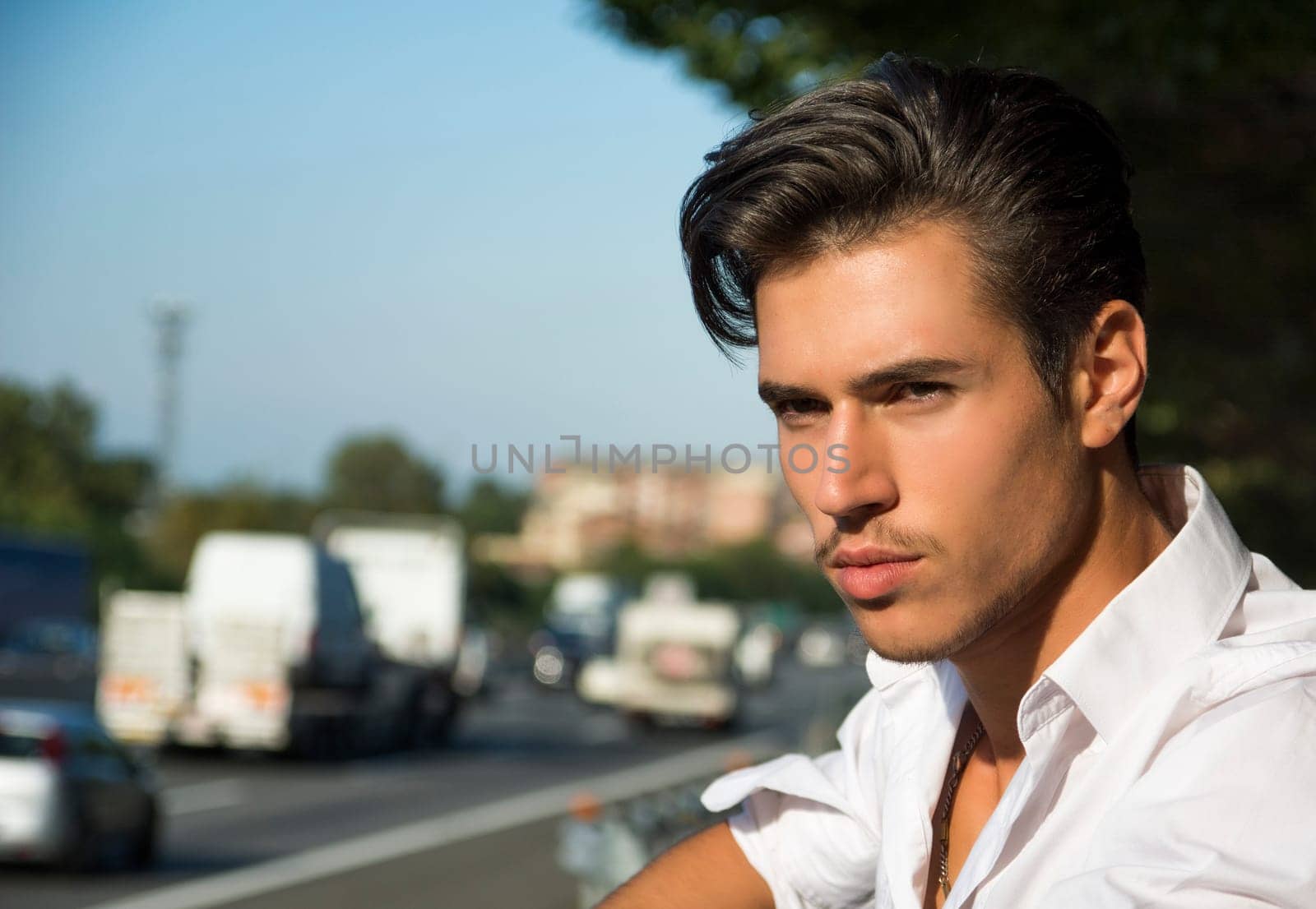 Handsome young man and road busy with cars and traffic in background