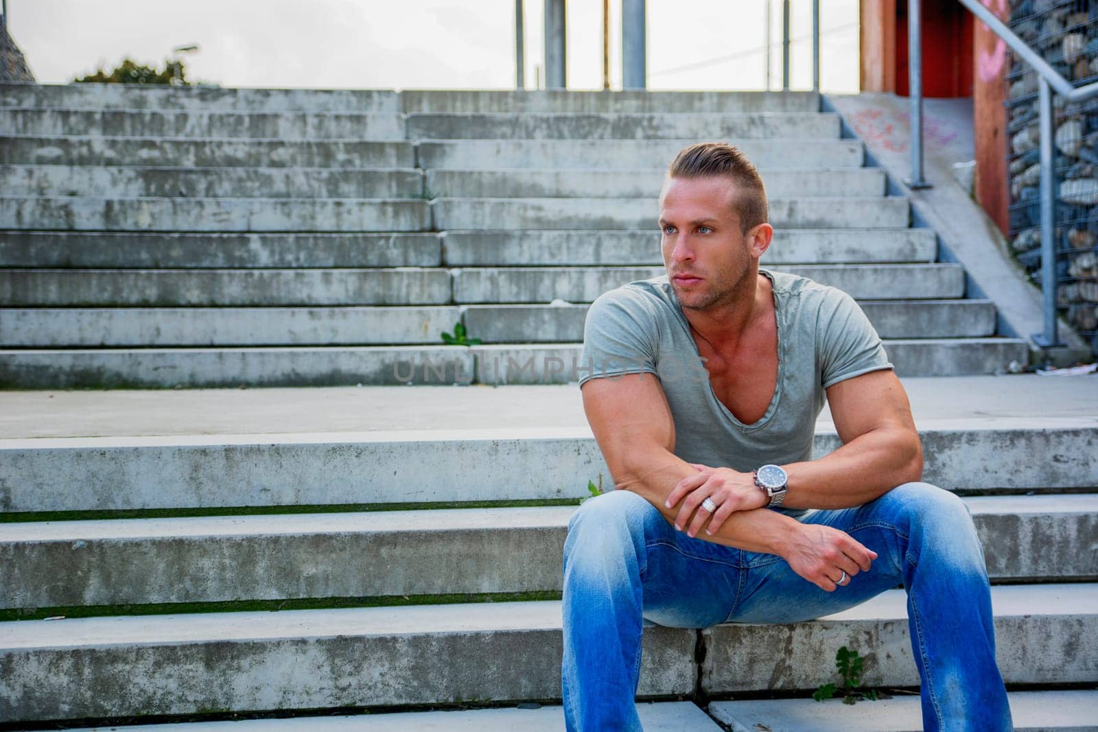 Handsome muscular blond man sitting on stair steps in city setting looking away
