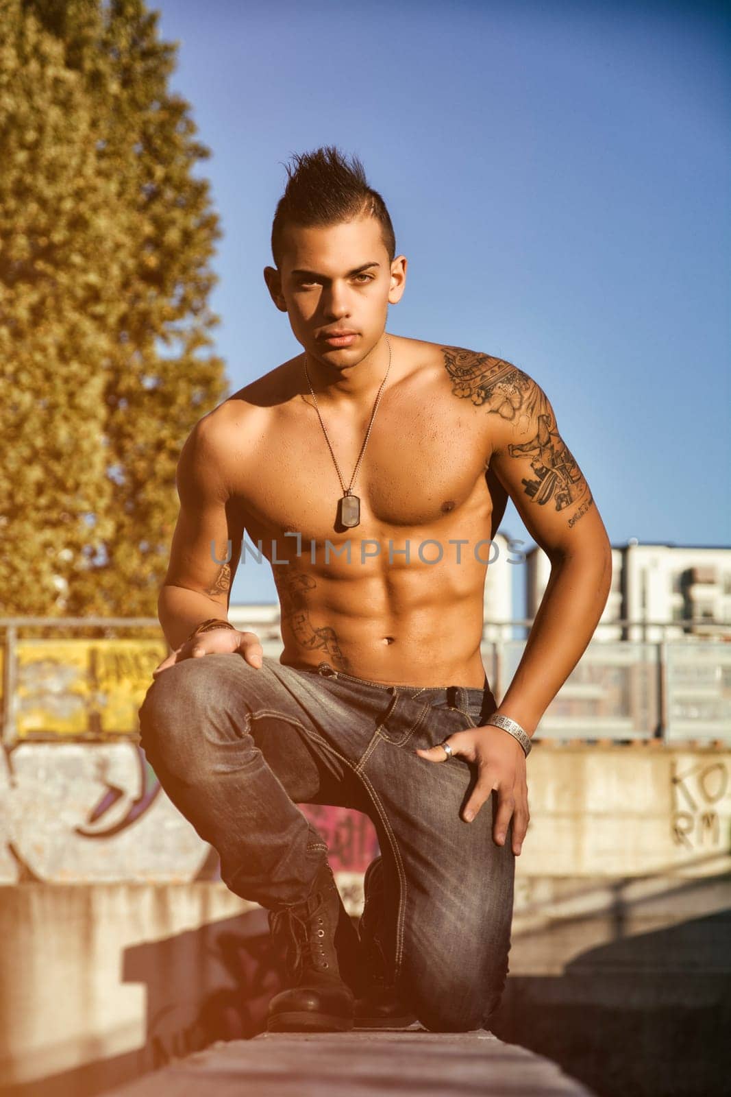 Handsome fit athletic shirtless young man in city setting kneeling on ground
