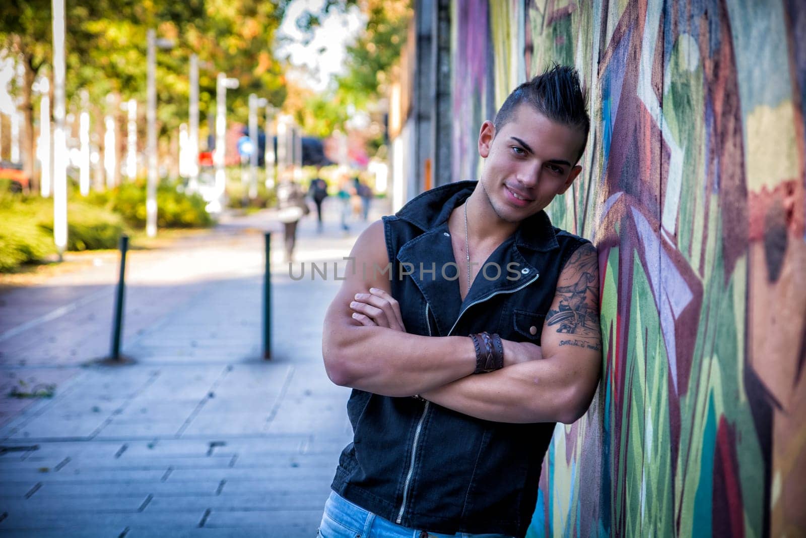 Handsome young man leaning against colorful graffiti wall, smiling at camera