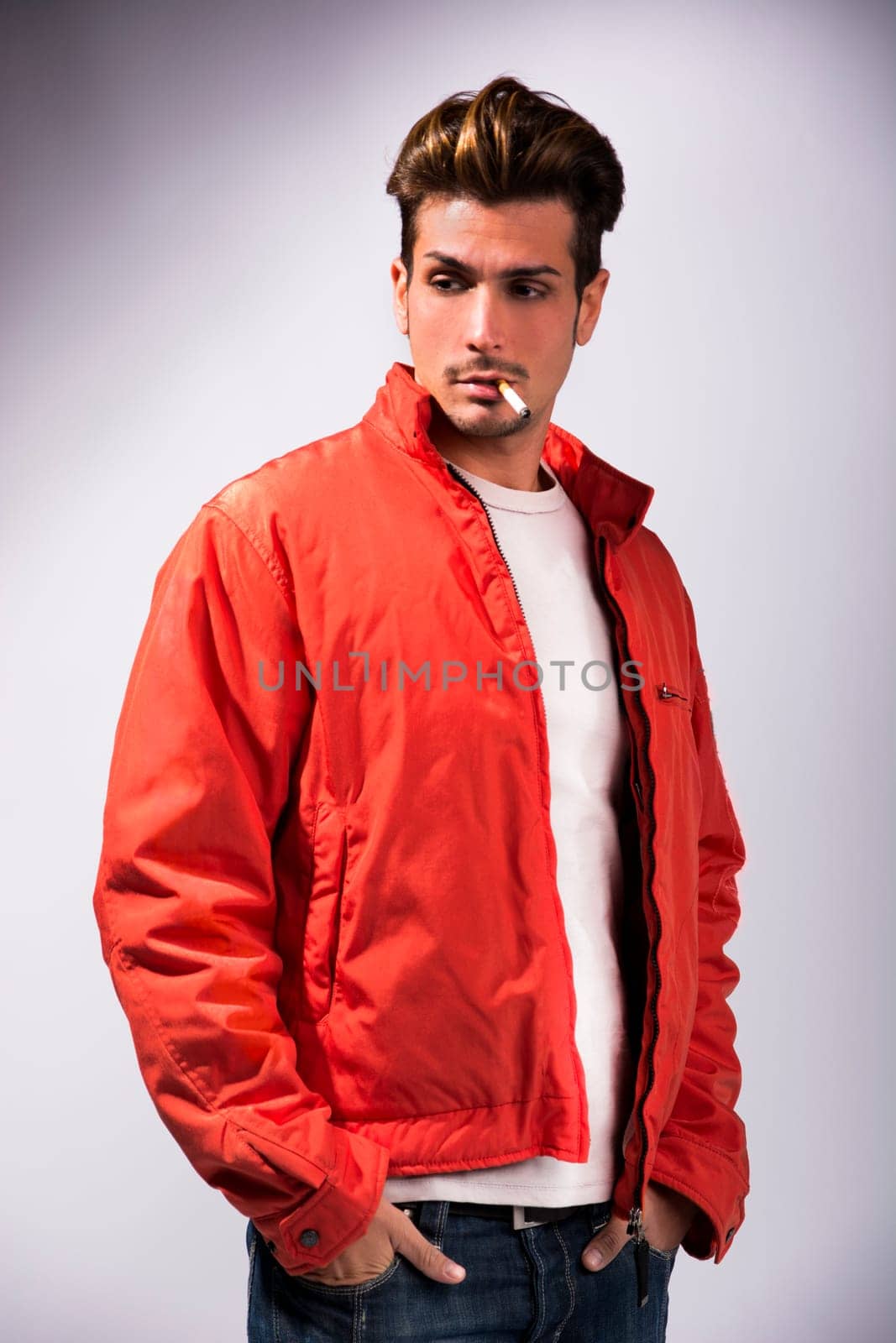 Handsome young man smoking cigarette, dressed as James Dean with red jacket on light background