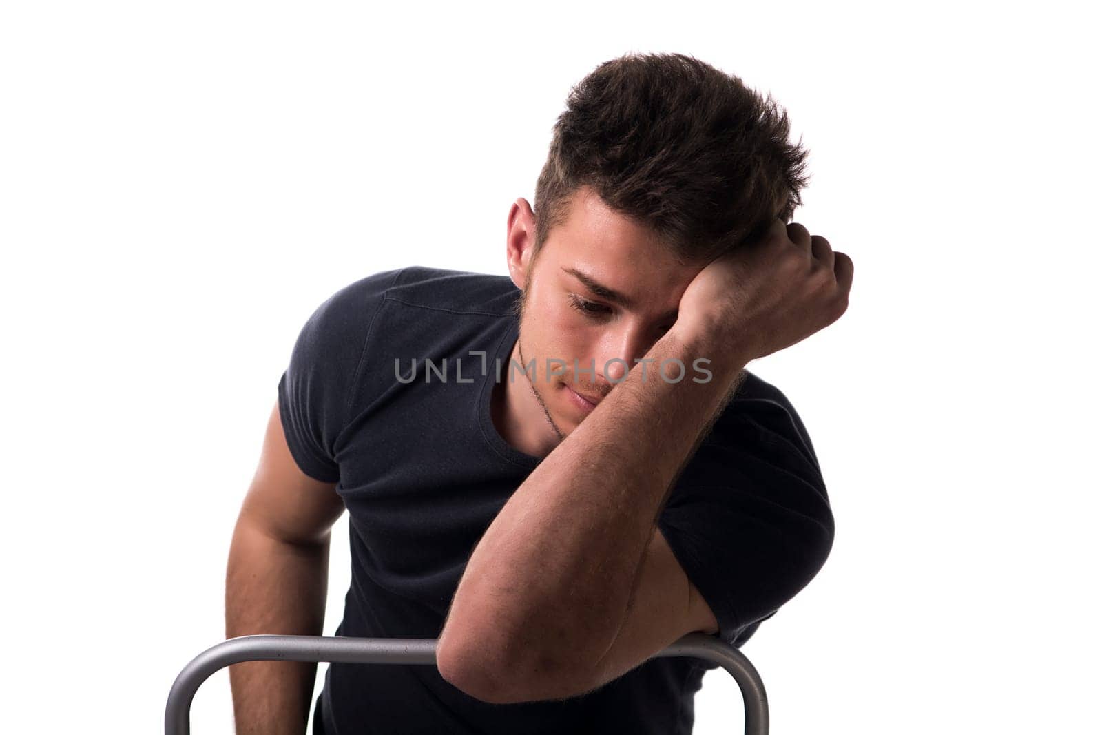 Attractive young man sitting, leaning on back of a chair looking down thinking, isolated on white