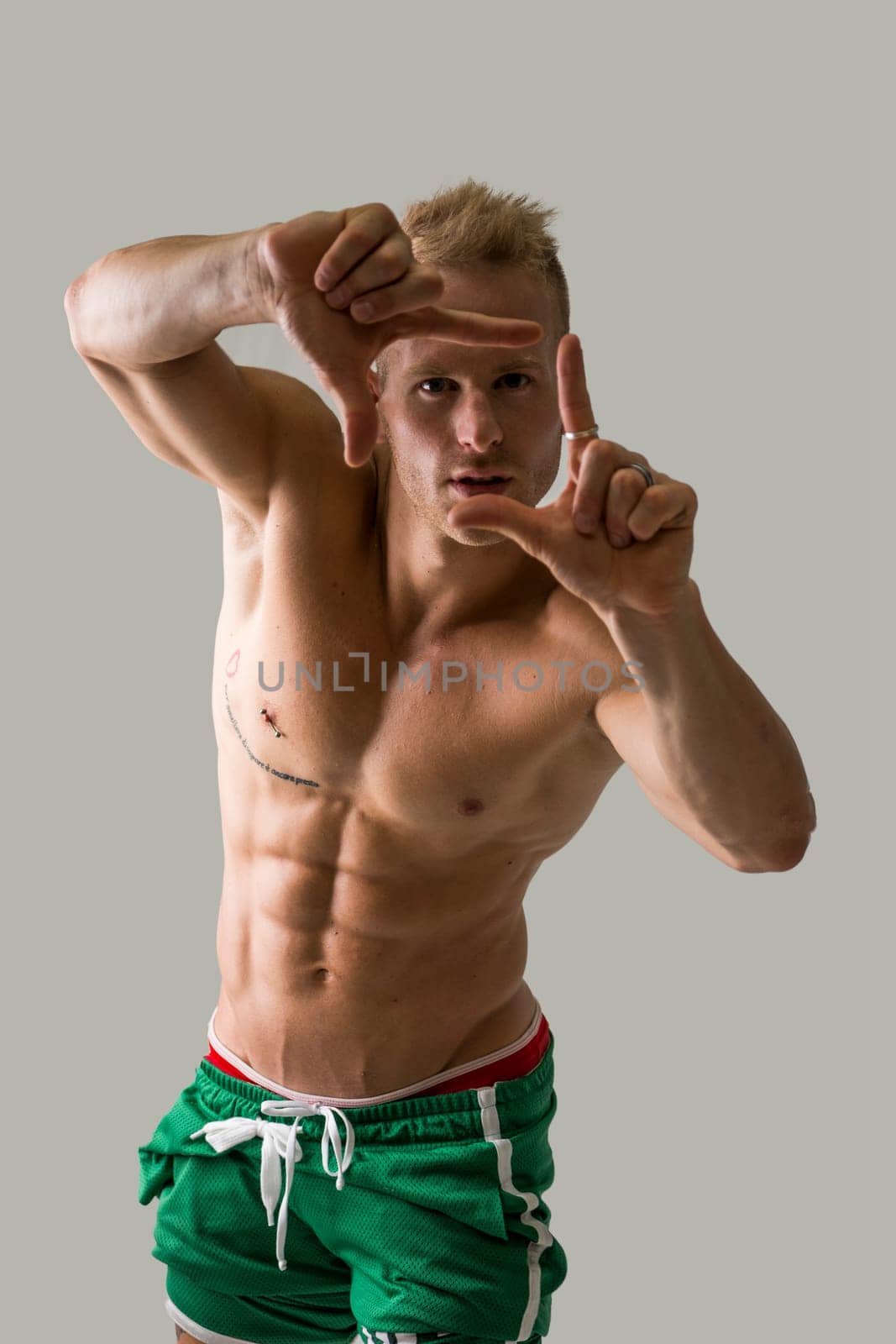 Handsome blond muscular shirtless young man doing frame gesture with fingers, looking at camera through it