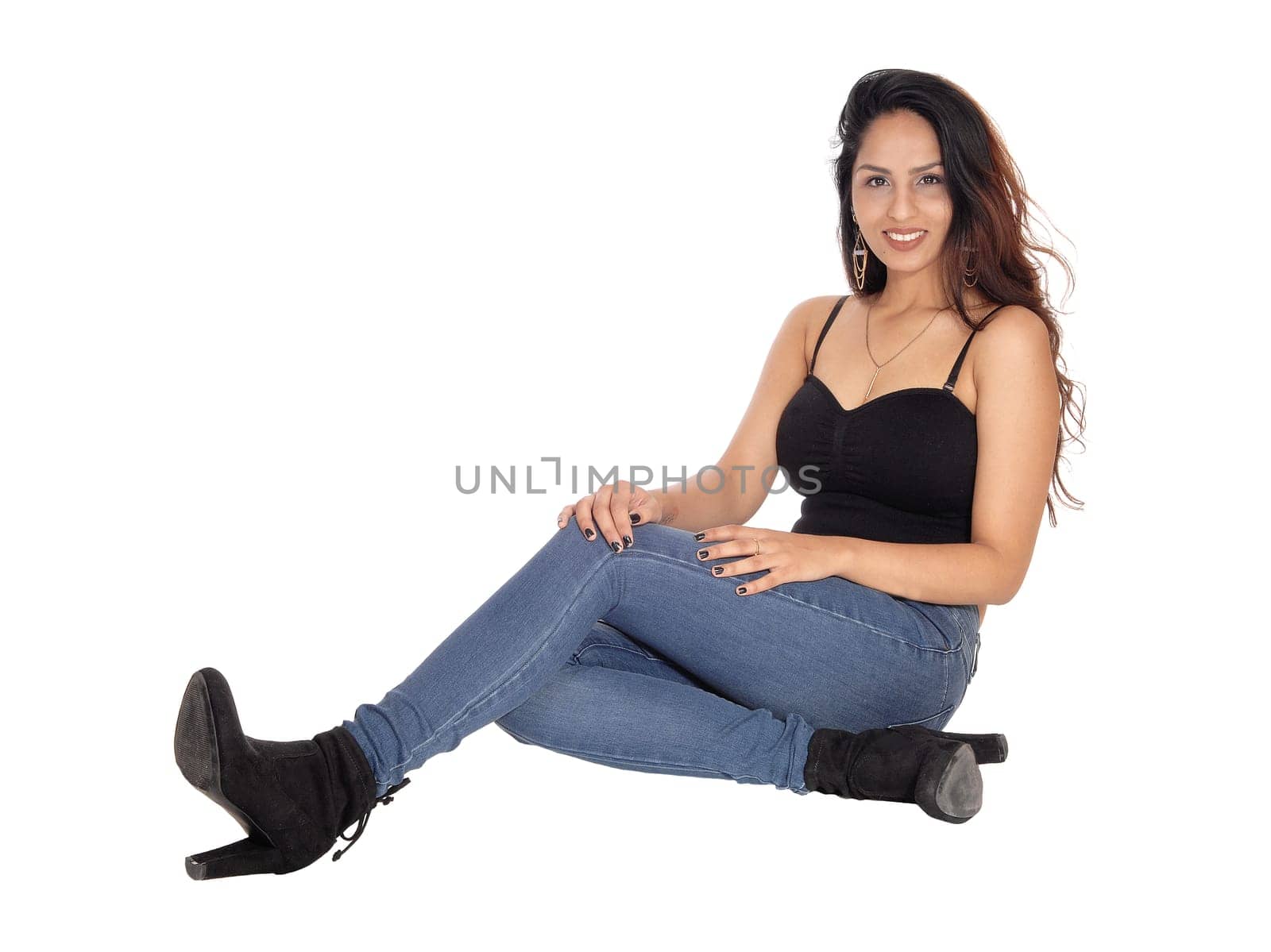 A beautiful slim young woman in jeans and a black corset sitting.on the floor, smiling, isolated for white background.