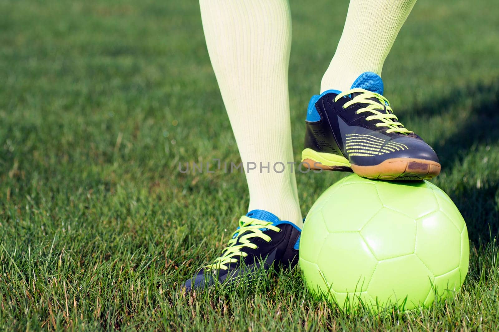 Legs of football player and football ball are on playing field, on the grass.