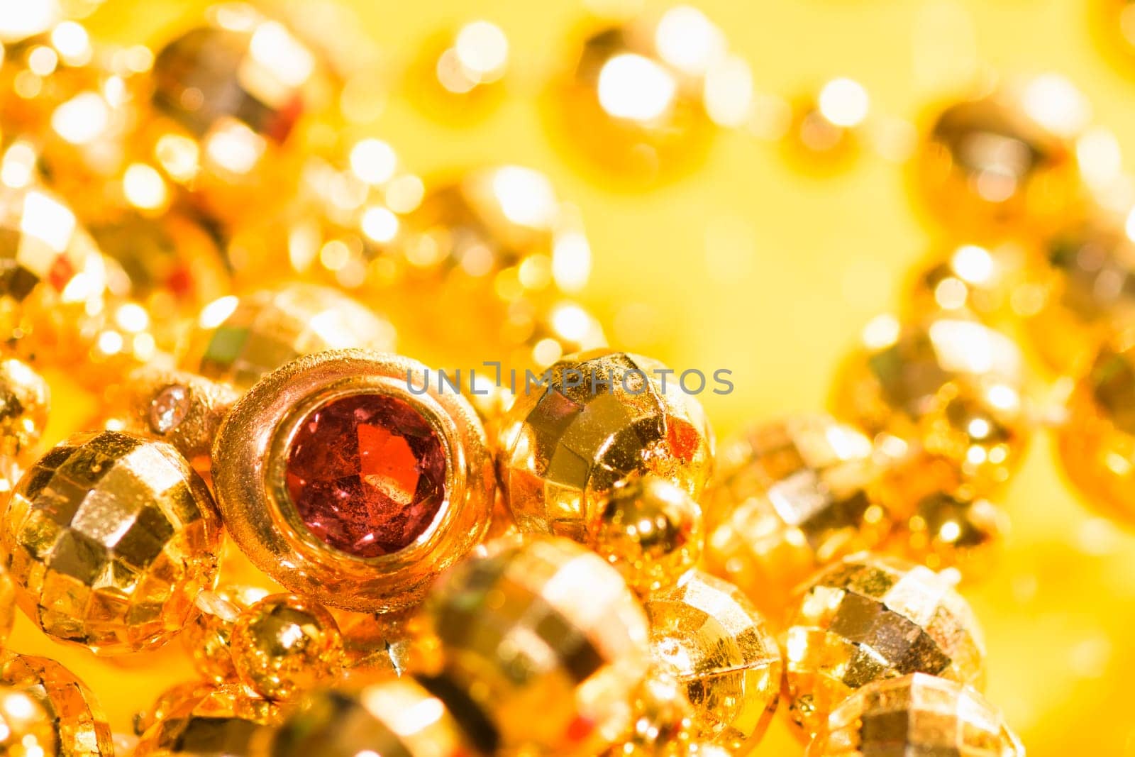 Golden jewelry and golden ring with gem are on yellow background.
