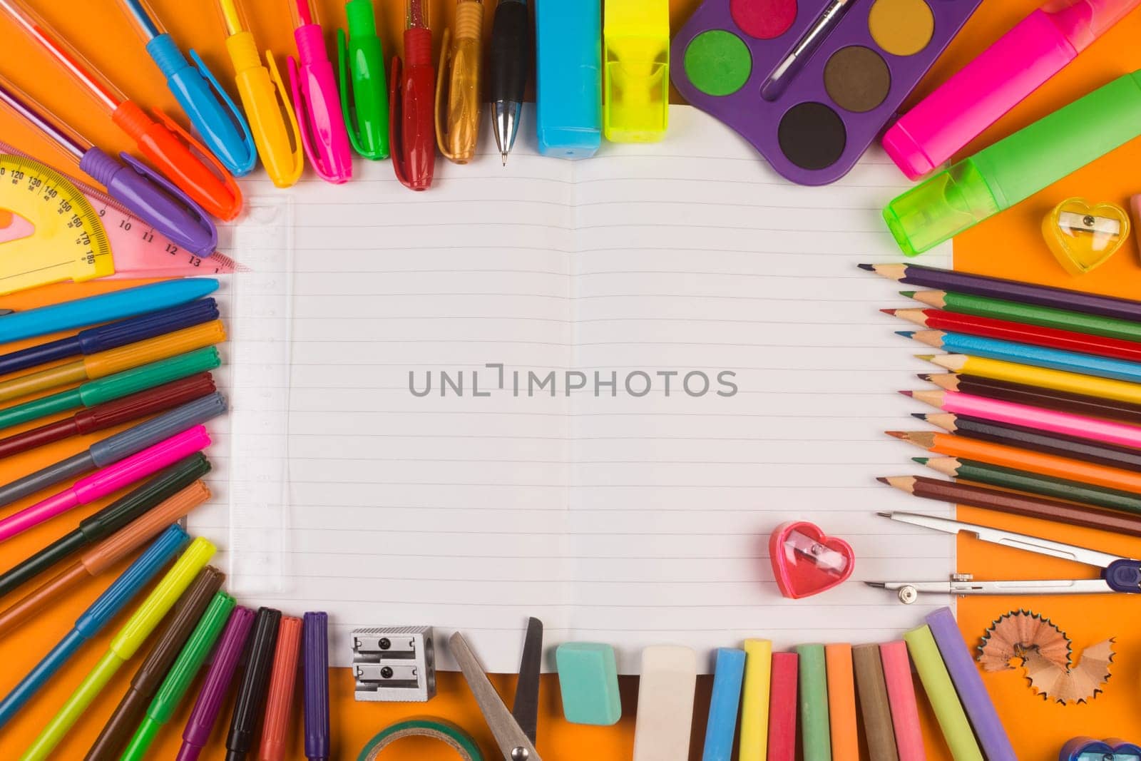 Different school supplies are on white blank notebook.