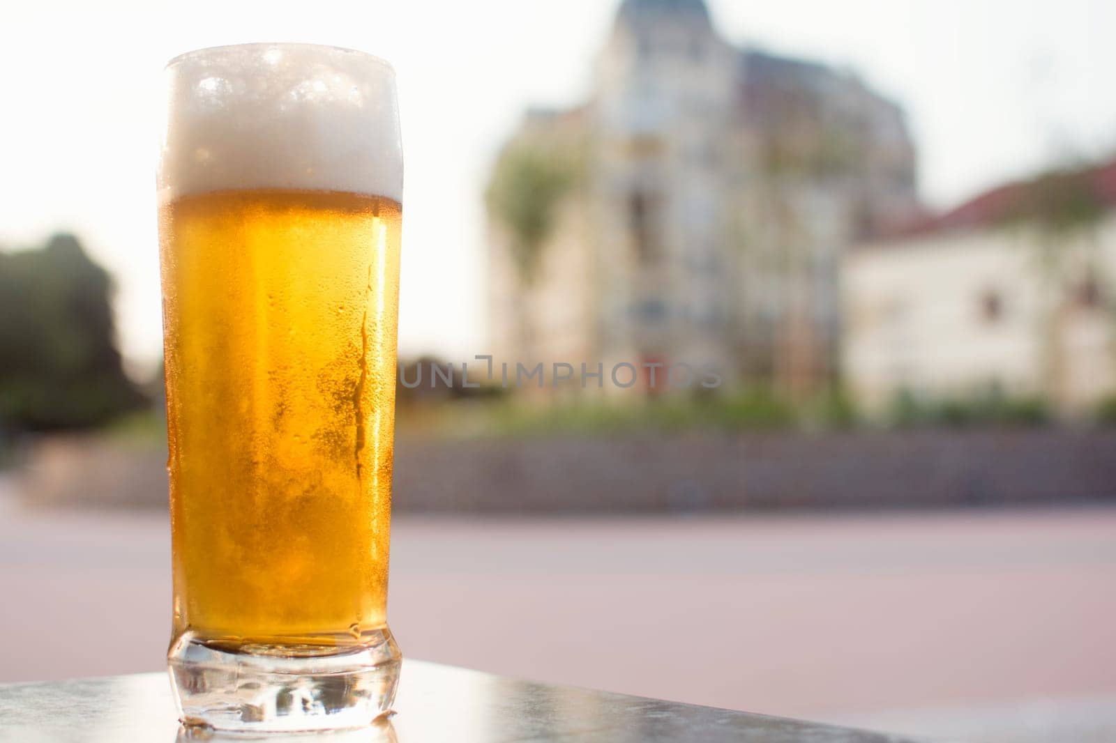 Cold light beer on table is on city background.