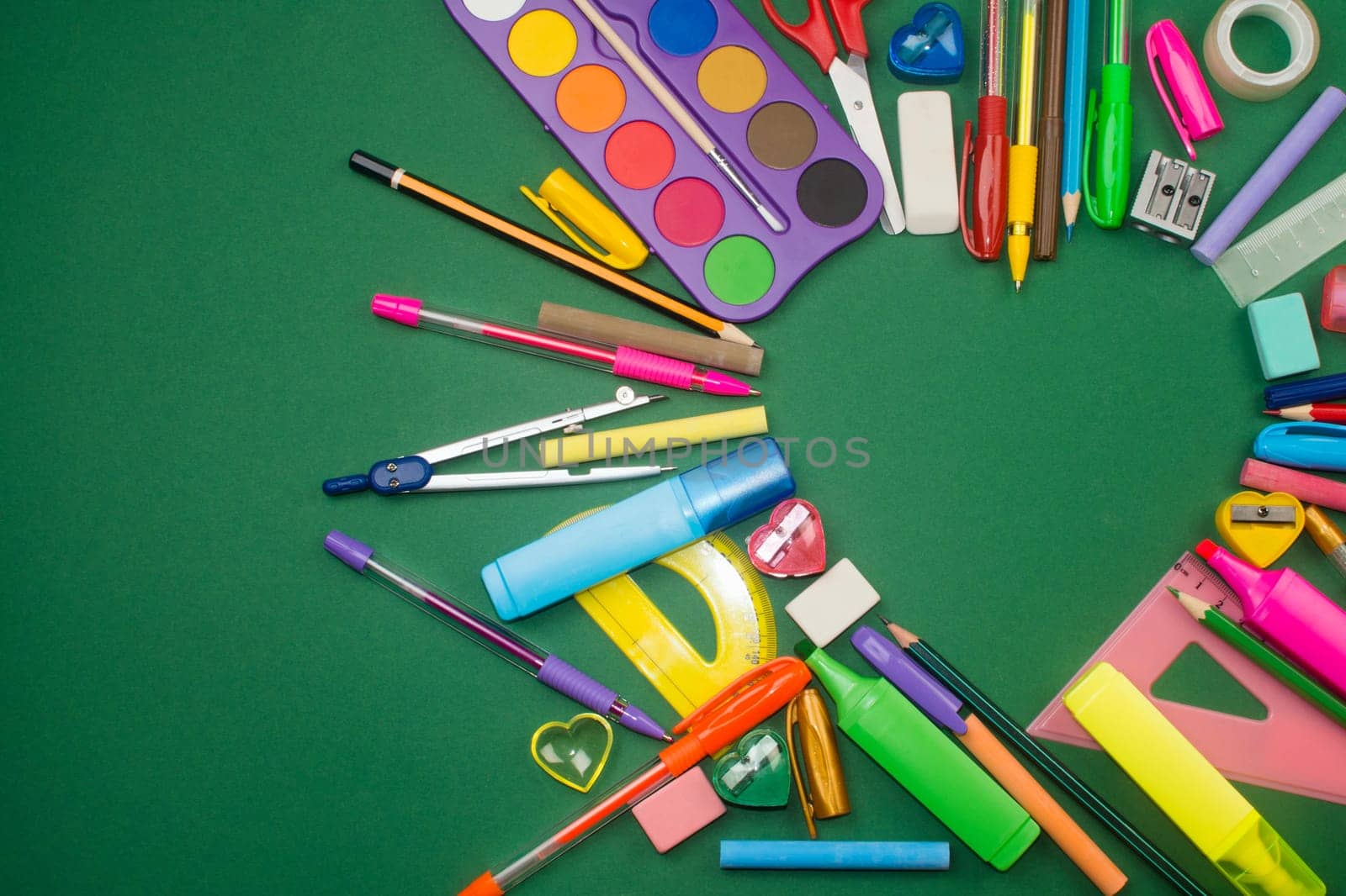 Different school supplies are in heart shape on green background.