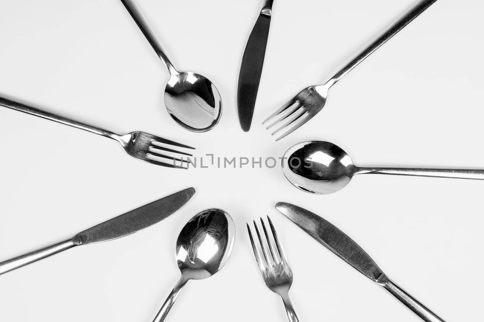 Silver cutlery, forks, knifes and spoons are around in circle on white background.