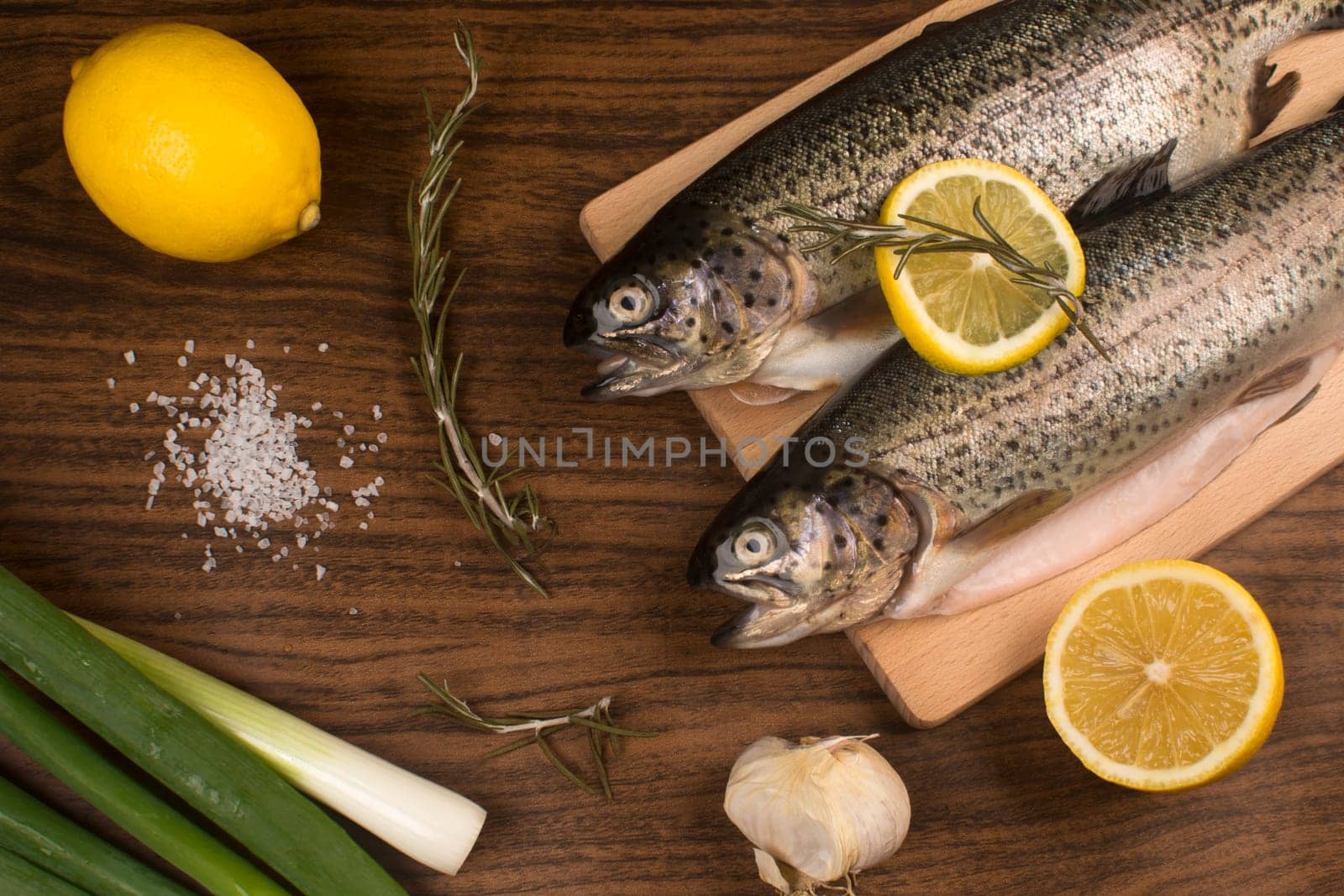 Raw trout fish with lemon, rosemary, garlic, salt and spring onion on brown wooden table.