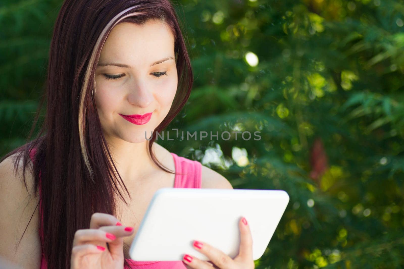 Young smiling woman with white digital tablet in nature.