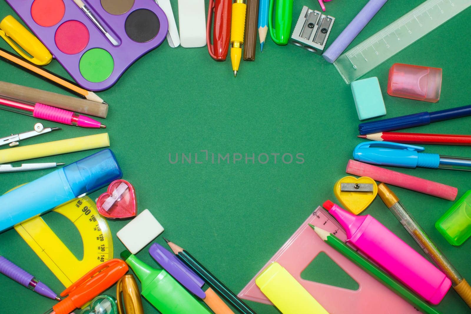 Different colorful school supplies in heart shape on green background.