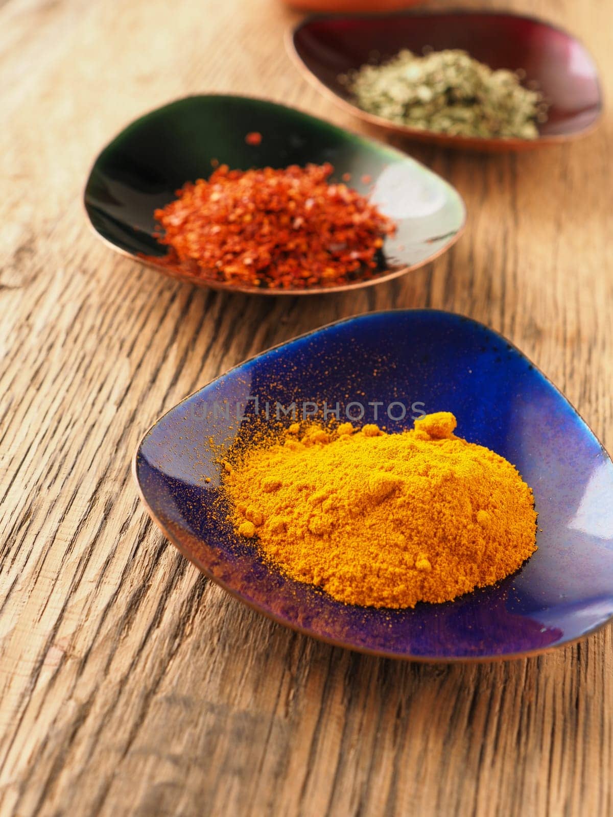 Assortment of different spices in colorful copper bowls on a rustic wooden table