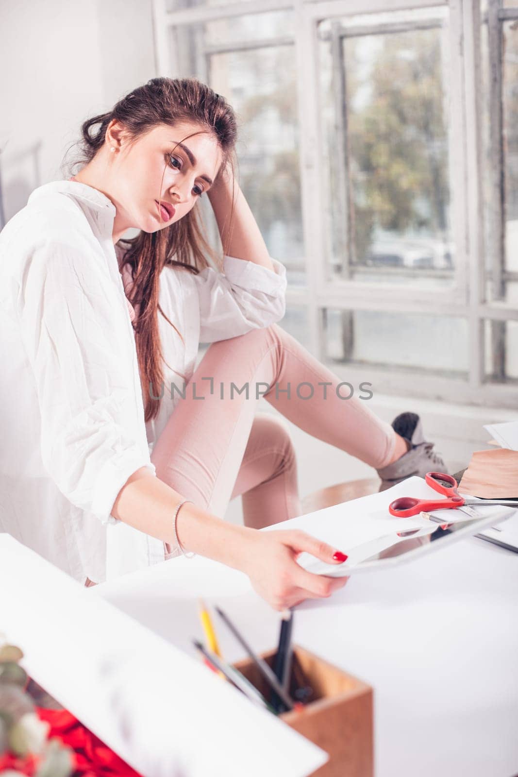 The female fashion designer working in studio sitting on the desk