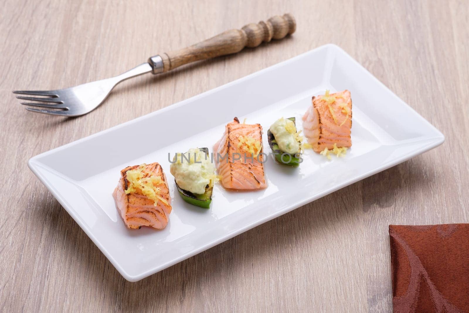 Salmon and avocado flamed with sauce and lemon zest on white plate