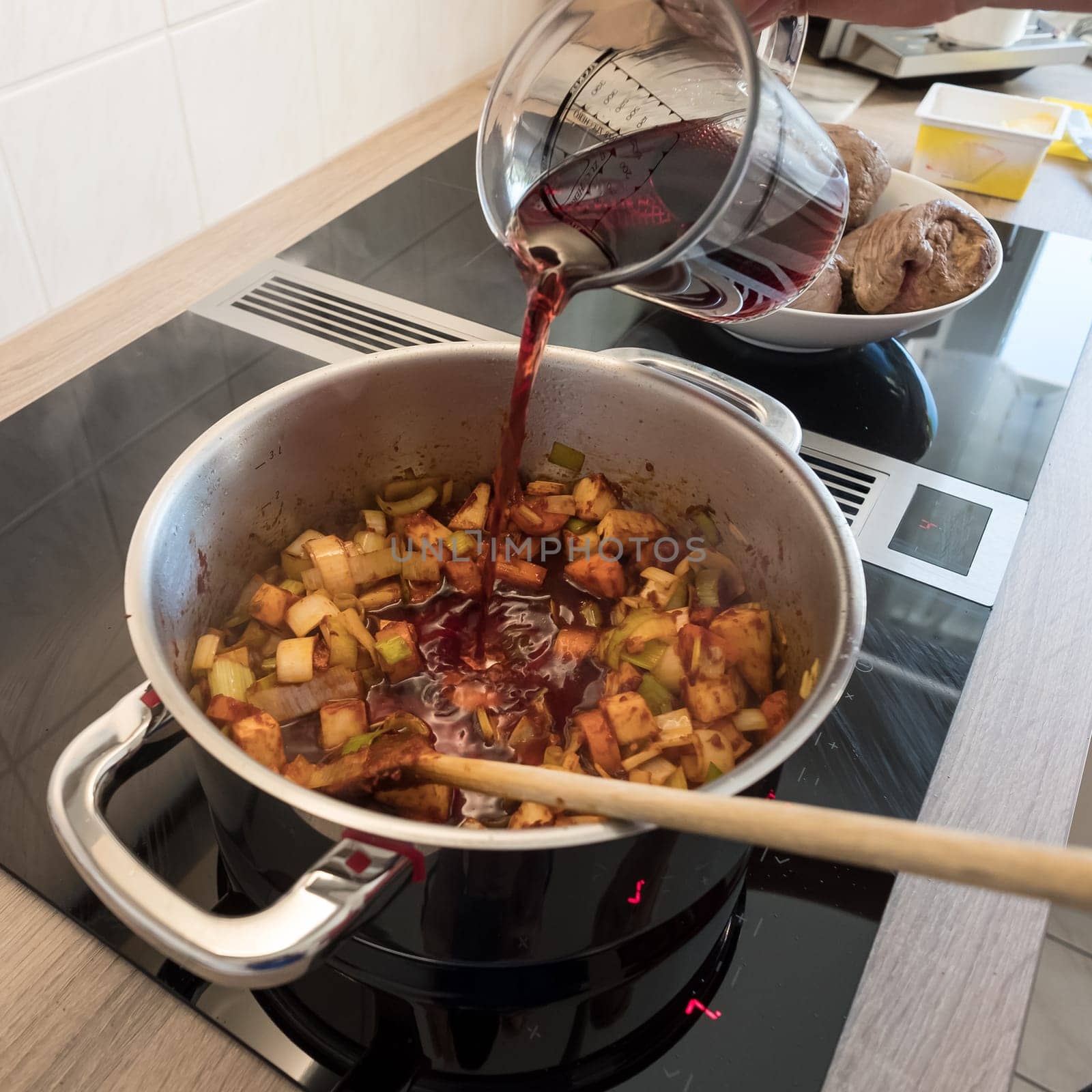 Female hand deglazes vegetables in the pot when frying with red wine