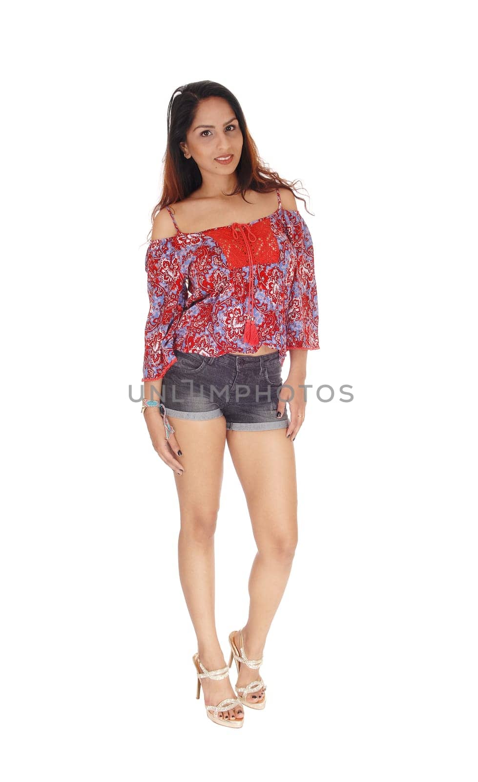 A slim young woman standing in shorts and colorful blouse from the.front in full length, smiling, isolated for white background.