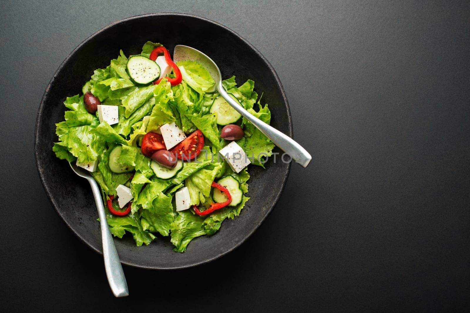Green salad with cheese and fresh vegetables on a black background. Greek salad.