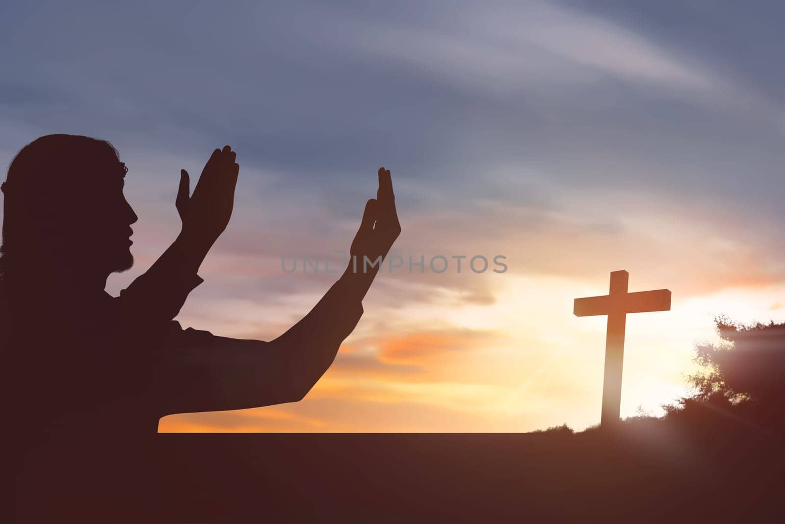 Silhouette man raising hand while praying to jesus on sunset background
