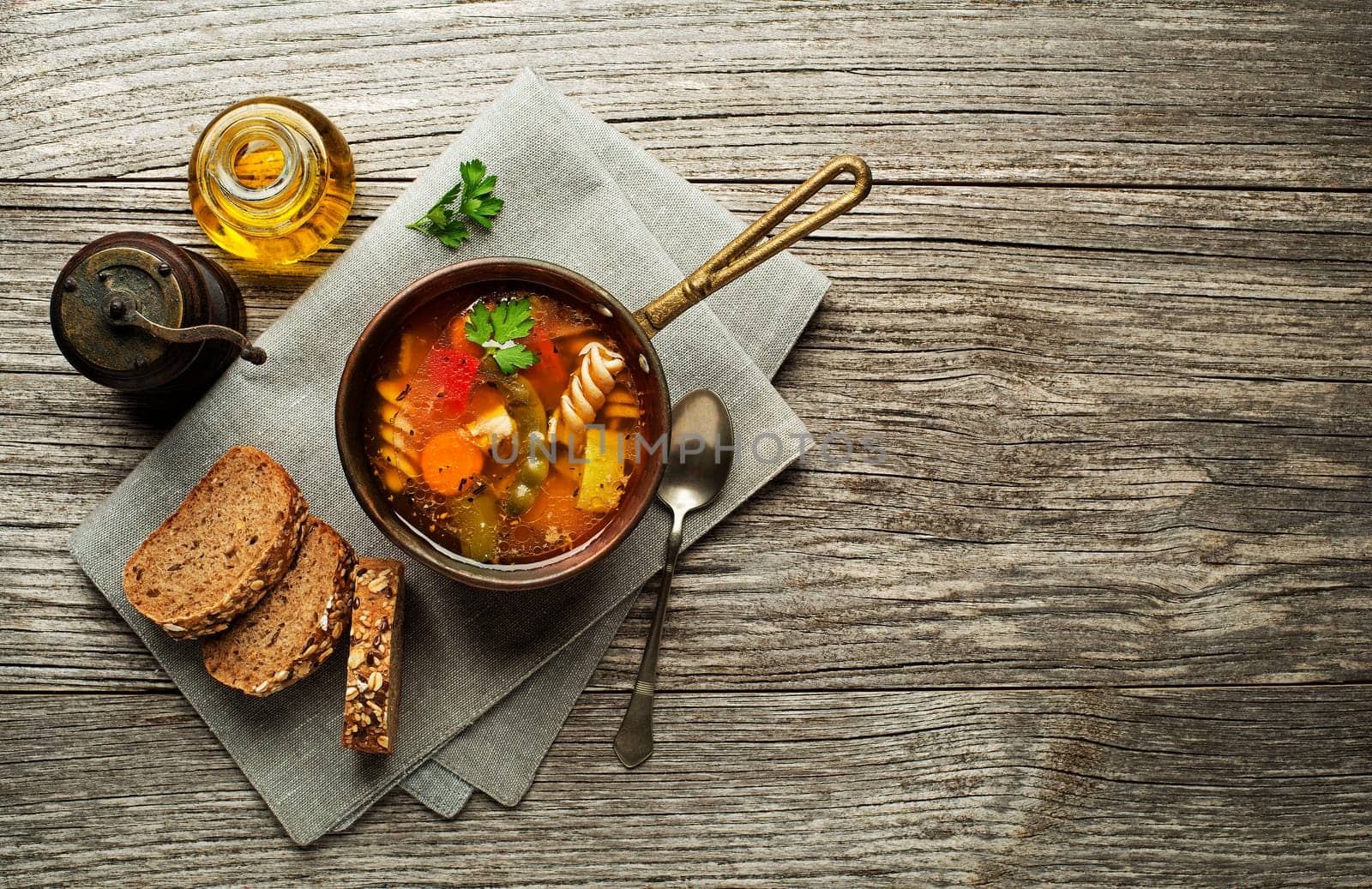 Pasta soup with vegetables and herbs on wooden background