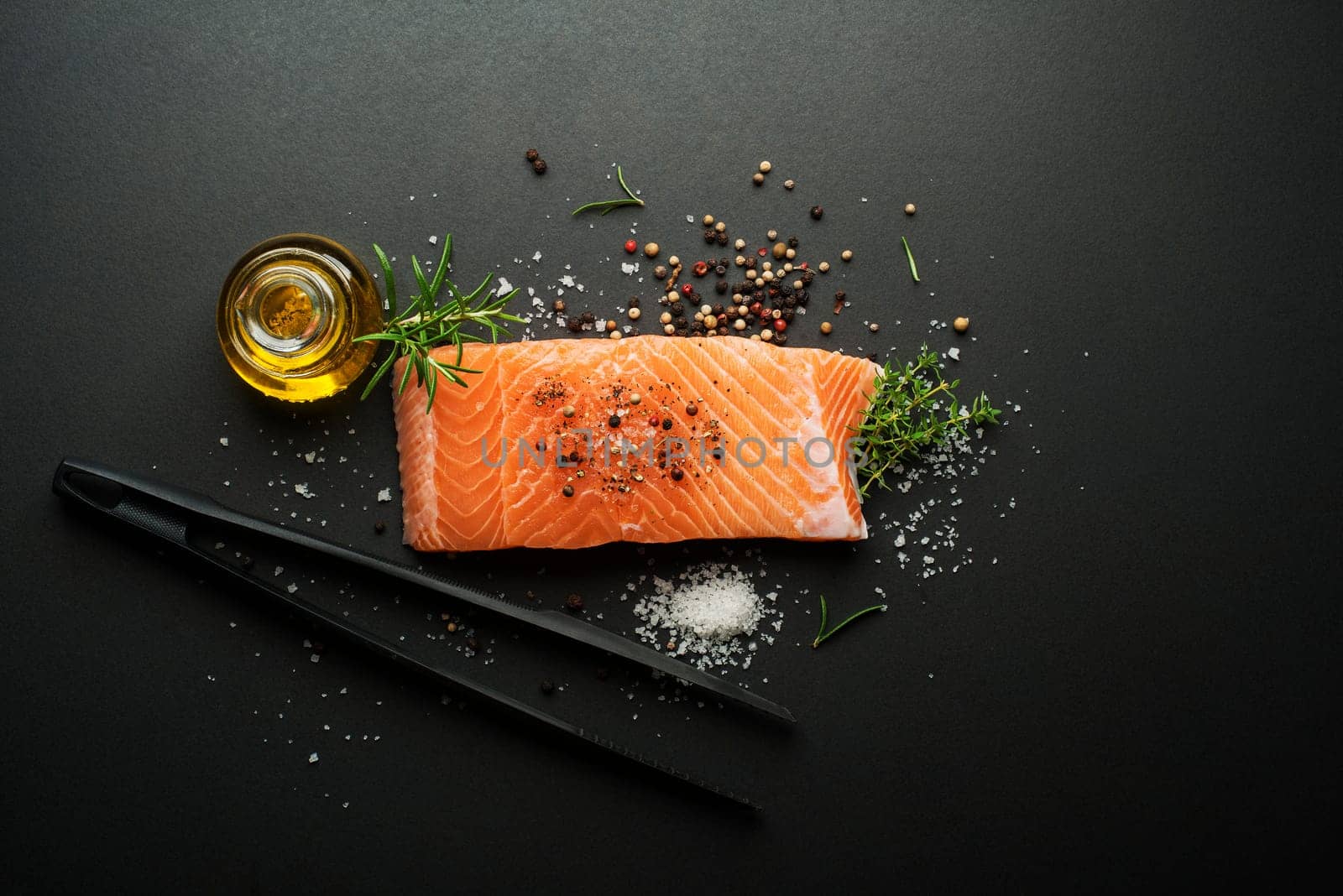 Raw steak of salmon fish with spices and herbs on black background