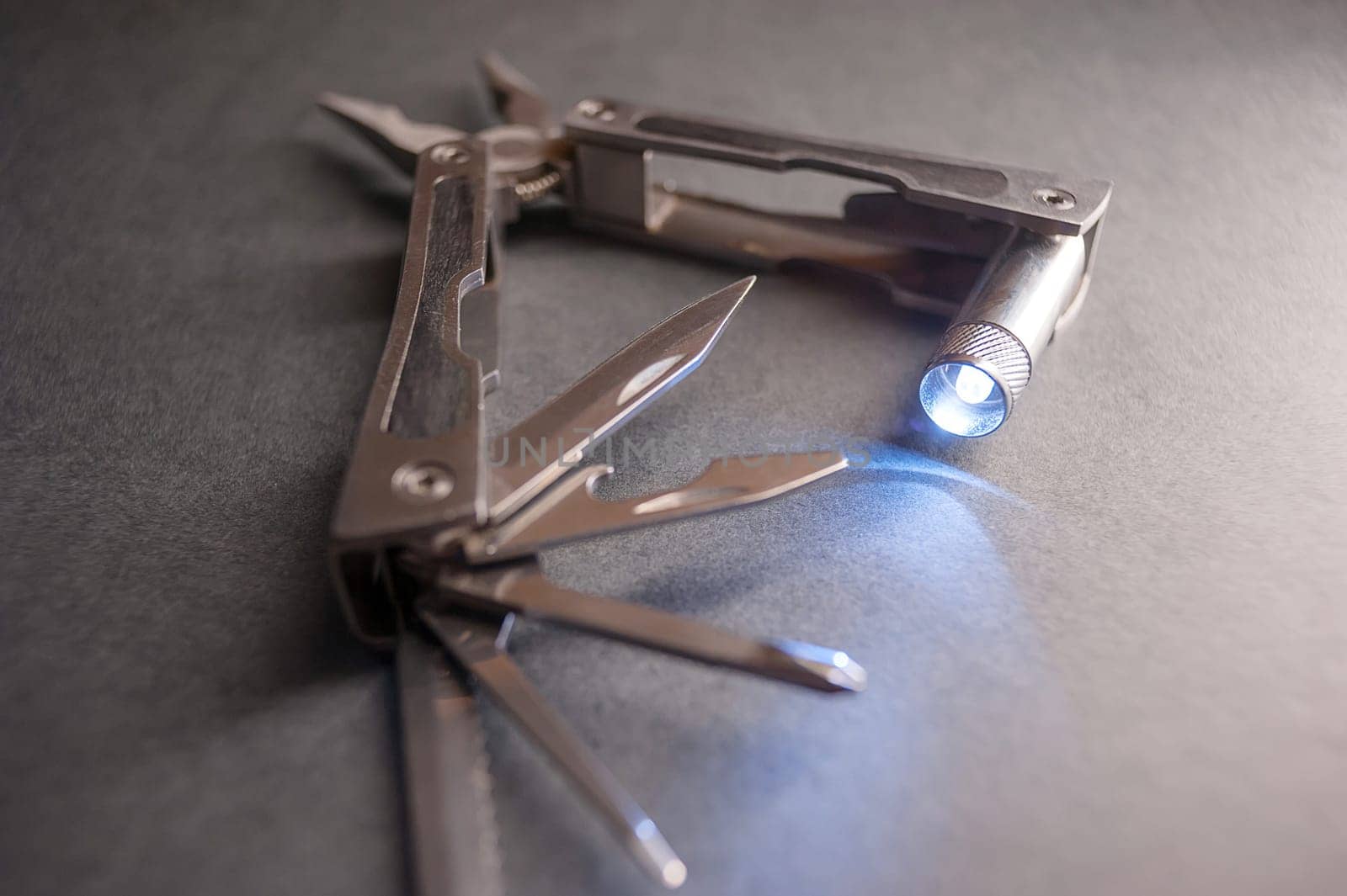 Combined pliers, multifunctional, with flashlight. Against the background of a gray texture.