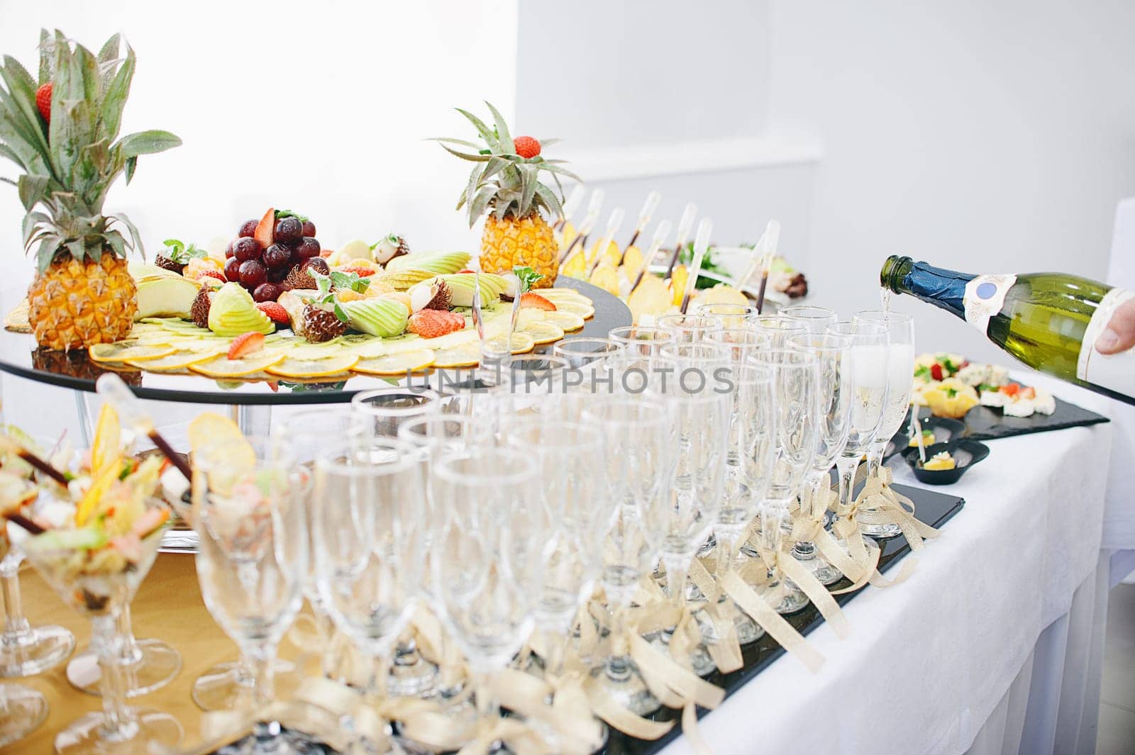 A beautiful fruit bar serving a festive table. The waiter pours champagne in wine glasses.